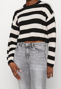 Černobílý pruhovaný krátký pletený svetr s kulatým výstřihem. Kombinováno se šedými džínami z denimu, klasického střihu a s mírně vypranou texturou.