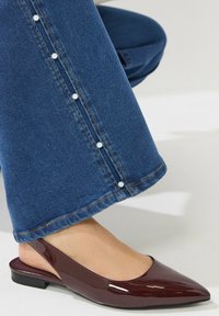 Burgundy patent slingback-kengät, joissa on teräväkärkinen muoto, yhdistettynä leveisiin sinisiin farkkuihin, joissa on valkoisia helmiä koristeena saumoissa.
