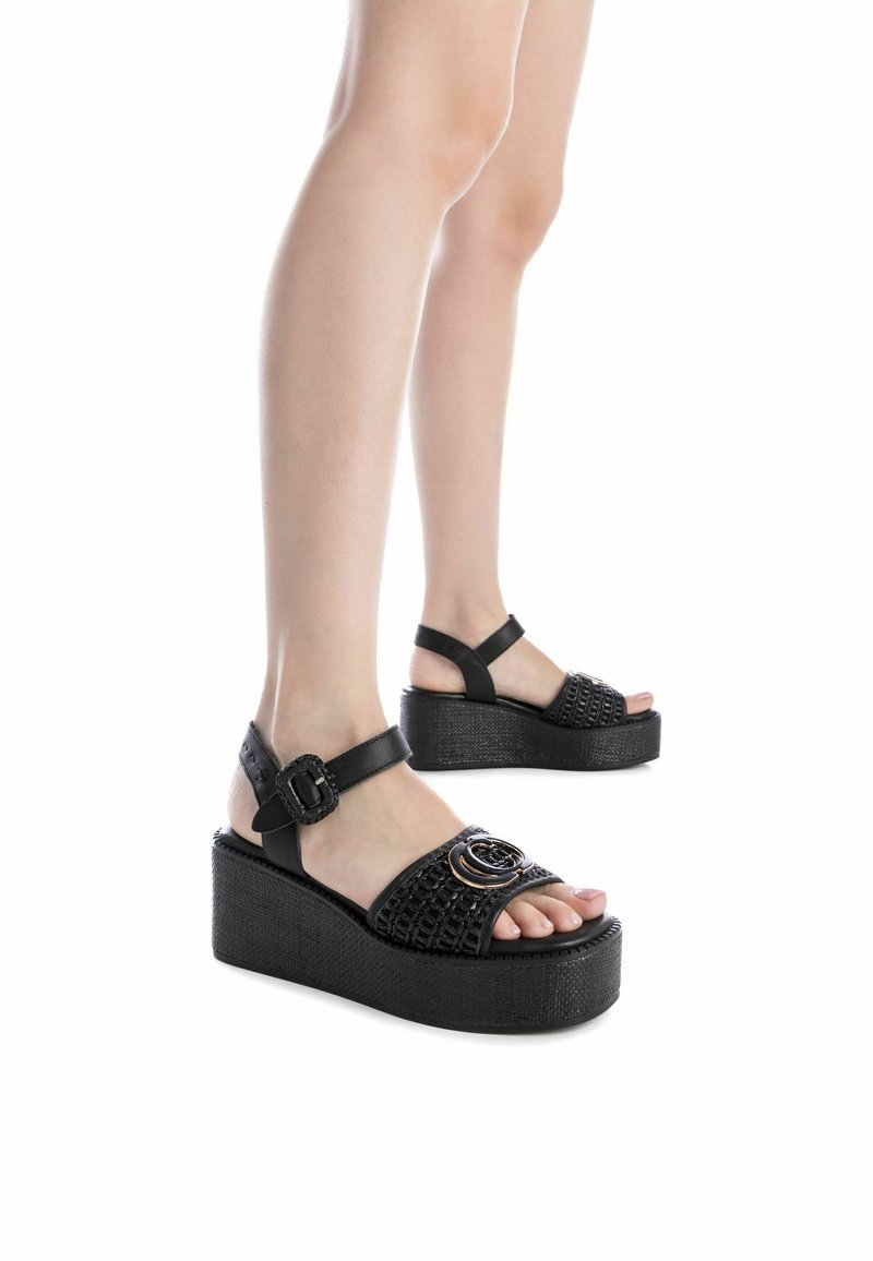 Sandali platform neri con texture intrecciata, cinturino con fibbia e un dettaglio circolare accentuato sul davanti. Suola in gomma con una base spessa.