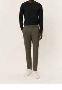 Černá košile s dlouhým rukávem, olivově zelené kalhoty s přiléhavým střihem a bílé tenisky. Oblečení má klasický design a hladký povrch.