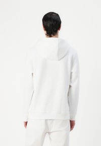 Sweat à capuche blanc, en tissu doux, coupe décontractée, avec des poignets et un ourlet côtelés. Design épuré avec une couture subtile, associé à un pantalon blanc.