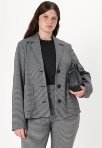 Svart og hvit hounds-tooth blazer med klippte revers, to frontlommer, tre knapper, parret med en stilren svart håndveske.