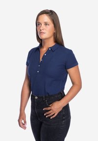 Marineblauwe polo met kraag, korte mouwen en een placket met drie knopen. Draagt deze met hoge taille zwarte jeans, die een strakke pasvorm uitstralen.