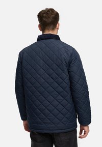 Chaqueta acolchada de color navy con cuello alzado y patrón de diamantes texturizado; cuenta con mangas largas y un corte holgado, adecuada para el uso casual.