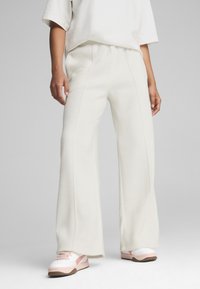 Pantalones de lana blancos de pierna ancha con costuras laterales, combinados con zapatillas deportivas rosas y blancas. Textura suave y ajuste relajado para mayor comodidad.