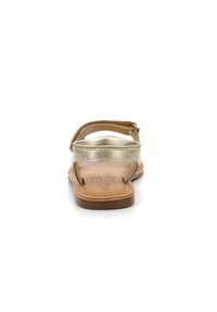 Sandalias planas metálicas doradas con suela de cuero marrón, correa ajustable en el tobillo y textura suave. Presenta marcas de la marca grabadas en la plantilla.