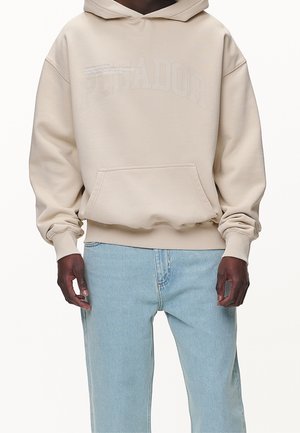 Beige hoodie met een voorzak, ribbelmanchetten en een reliëflogo. Gecombineerd met lichtblauwe jeans. Gemaakt van katoen.