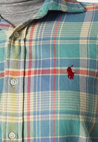 Rutigt knapp-up skjorta i blå, grön och gul nyanser med r öda accenter, mjukt tyg och en liten röd hästlogotyp på bröstet.