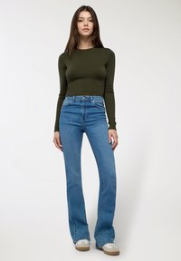 Oliwkowa, długRękawowa bluzka w połączeniu z dżinsami o wysokim stanie i rozszerzanymi nogawkami w odcieniu niebieskim. Tkanina ma gładką teksturę; dżinsy mają subtelne szwy i kieszenie.