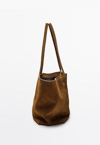 Bruine suède tote bag met twee lange handvatten, een zachte textuur en een gebogen vorm. Heeft contrasterende stiksels en een open bovenkant.