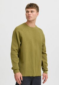 Hanorac cu mânecă lungă de culoare verde măsliniu, cu guler tip crew și manșete ribbate, având o croială lejeră și un material texturat.