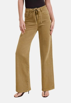 Frau trägt weite beige Hose mit Kordelzug in der Taille und Taschen, kombiniert mit schwarzen Sandalen mit Absatz und einem schwarzen Top.
