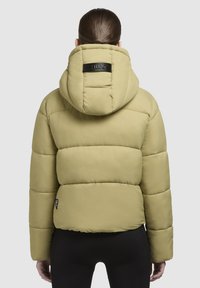 Jachetă puf vârtoasă de un verde măsliniu deschis, cu glugă detașabilă, având cusături orizontale și un etichetă mică cu logo pe partea stângă.