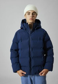 Marineblå boblejakke med glidelåslukking og hette, med tykk polstring, glatt tekstur og ribbet hvit lue.