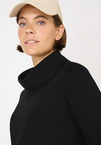Zwarte top met een kolknek, zachte stof en lange mouwen. Draad met een lichtgekleurde pet, heeft een gladde textuur en minimale details.