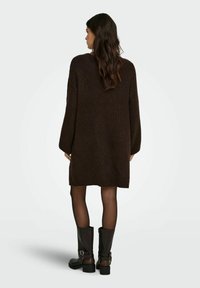 Brązowa dzianinowa sukienka swetrowa o luźnym kroju, z długimi rękawami i prążkowanym wykończeniem na dole. Połączona z czarnymi kozakami za kolano z ozdobnymi klamrami.