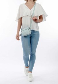 Borsa a tracolla trapuntata di colore azzurro chiaro realizzata in materiale sintetico con chiusura a zip, indossata sopra una blusa bianca a volant e abbinata a jeans slim.