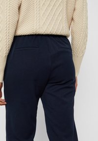 Navy blue pants with a soft texture and elastic waistband, featuring two back pockets. Worn with a cream cable-knit sweater.