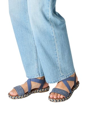 Feet wearing blue woven sandals with crisscross straps and light blue denim jeans visible from mid-calf down.