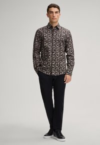 Camicetta nera con un motivo a spirale crema e rosa, colletto a bottone, vestibilità slim, abbinata a pantaloni neri e scarpe basse nere.