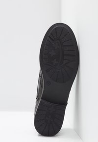 Baskets noires avec une semelle à motif, une tige lisse avec des perforations pour la respirabilité, et un design profilé bas. Taille indiquée : 37.