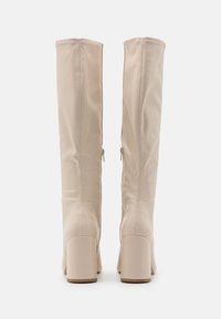 Knähöga beiga stövlar i slät tyg med klack, som har en dragkedja på utsidan för enkel påtagning.