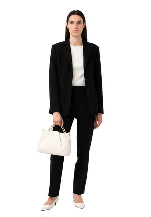 Blazer nero su una maglietta bianca, abbinato a pantaloni neri, borsa bianca e tacchi color crema con design a punta.