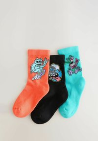 Tres pares de calcetines de tripulación en naranja, negro y azul verdoso. Cada uno presenta gráficos de dibujos animados únicos: un patinador, un personaje con gorra y otro en un patinete.