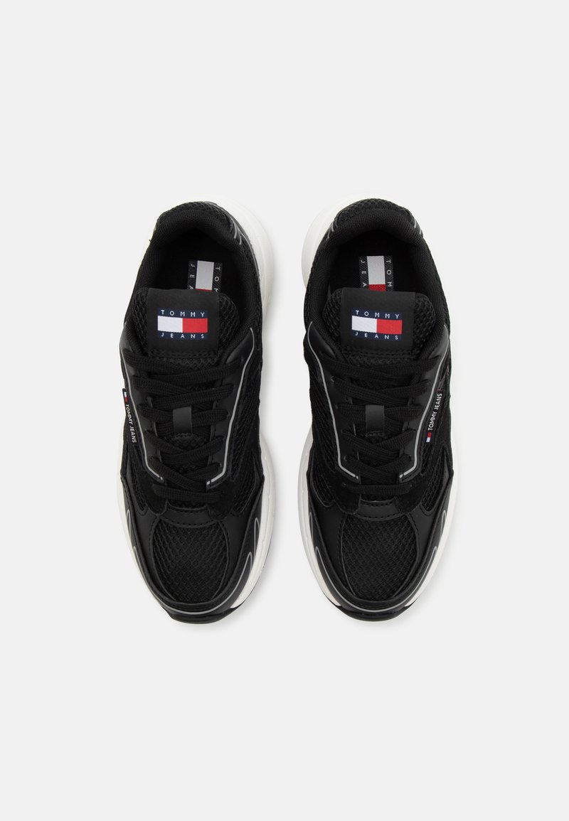 Chaussures de sport noires en mesh et cuir, avec un design à lacets, présentant des accents blancs et le logo Tommy Jeans sur la languette et le côté.