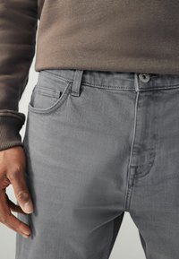 Jeans in denim grigio con fit slim, dotati di tasca frontale e chiusura con un singolo bottone. Il materiale ha una texture liscia e dettagli di cucitura discreti.