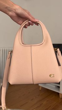 Μικρή δομημένη τσάντα χειρός από υφή ροζ δέρμα, με στρογγυλή λαβή στην κορυφή, χρυσά αξεσουάρ και σημαία λογότυπο.