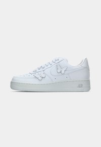Hvite lavtopp sneakers med to sommerfuglformede dekorelementer på siden og "AIR" merkevare på sålen.