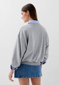 Grå sweatshirt med sænkede skuldre og ribbede manchetter lagdelt over en blå stribet skjorte med krave, parret med en denim mini nederdel.