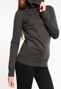Pullover a collo alto grigio scuro a maniche lunghe in tessuto morbido, con una vestibilità aderente e polsini a costine, indossato con pantaloni neri.