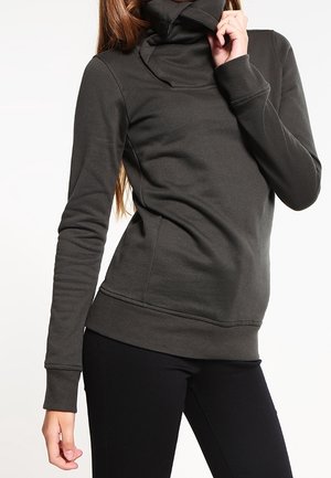 Pulóver de cuello alto de manga larga en gris oscuro, confeccionado en una tela suave, con un diseño ajustado y puños acanalados, combinado con pantalones negros.