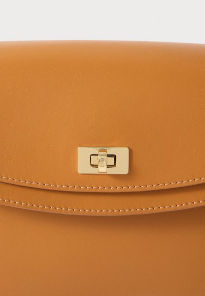 Tan leren handtas met een gladde textuur, voorzien van een gouden rechthoekige sluiting en contrasterende randstiksels. Eenvoudig en strak ontwerp.