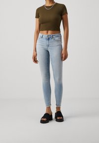 Ljust blå skinny jeans med fransar i nederkant, kombinerat med en mörk olivgrön crop-top och svarta plattformssandaler. Silvrig kedja som halsband.