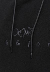 Zwarte fleece hoodie met een tonal logo, trekkoorden met plastic punten en een zachte textuur. Minimalistisch ontwerp zonder duidelijke patronen.