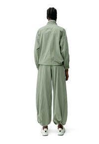 Zelený ľahký dvojdielny outfit s voľnými nohavicami a zodpovedajúcou bundou. Obsahuje elastické manžety a golier. Nosí sa s bielymi topánkami.