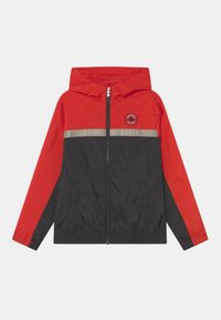 Rød og sort vindjakke med hætte, front lynlås, to sidelommer og en lys grå stribe med teksten "CONVERSE ALL STAR".