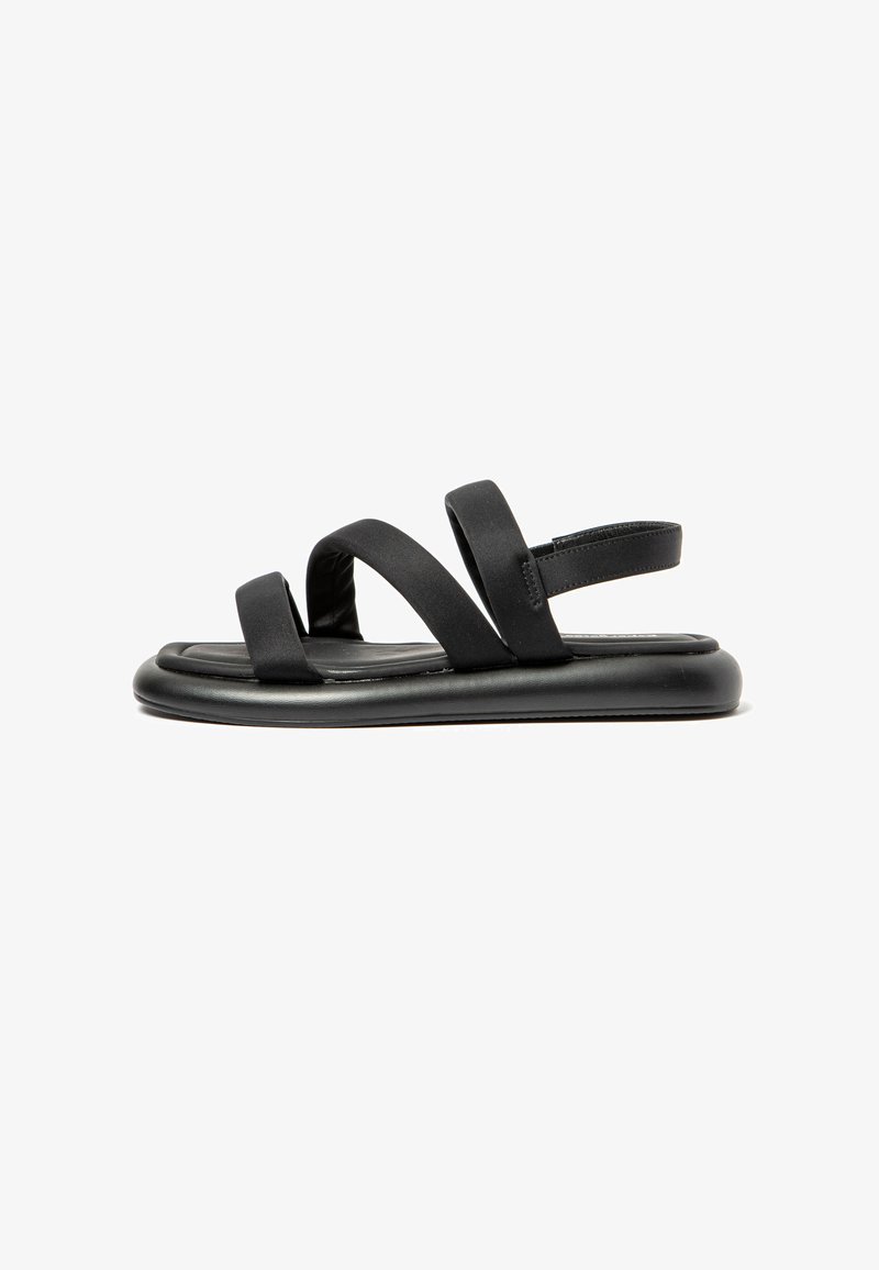 Black sandals with a flat sole, featuring two wide, soft straps and a narrow heel strap for secure fit. Smooth material with no patterns.