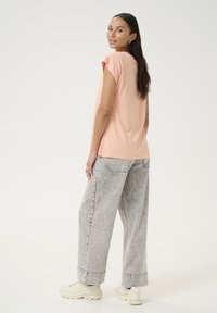 Chemise rose pâle à manches courtes associée à un jean gris, ample. La personne porte des baskets crème, mettant en avant une tenue décontractée et relaxée.