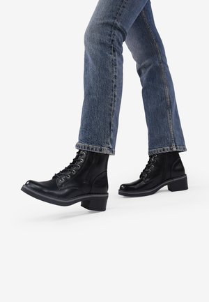 Black leather lace-up ankle boots with a rounded toe, block heel, and textured sole, worn with blue denim jeans.