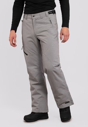 Pantalones de nieve grises con un corte relajado, múltiples bolsillos con cremallera y puños reforzados, combinados con calzado negro.