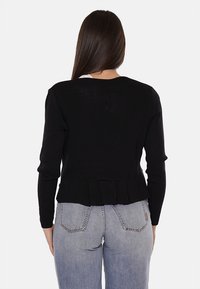 Maglietta nera a maniche lunghe con texture a costine e design plissettato sul retro, abbinata a jeans azzurri a vita alta con tasche posteriori.
