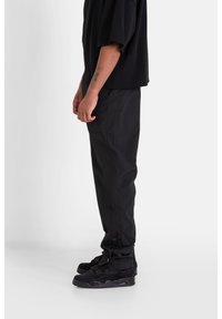 Svart överdimensionerad t-shirt med korta ärmar, tillsammans med svarta slim-fit byxor och svarta sneakers. Materialet verkar slätt utan synliga mönster.