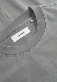 Tricou gri din bumbac, cu guler rotund, guler ribbed și etichetă cu "GABBA". Materialul are o textură netedă și un design minimaliste.