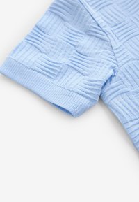 Vaaleansininen teksturoitu neulepaita, jossa on resorikahleet ja kuvioitu malli, jossa on geometrisia muotoja ja viivoja.