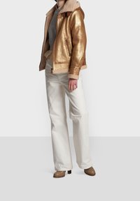 Metallic gold jacket with a shearling collar, paired with white pants and brown boots. Features zip closure and side pockets.
