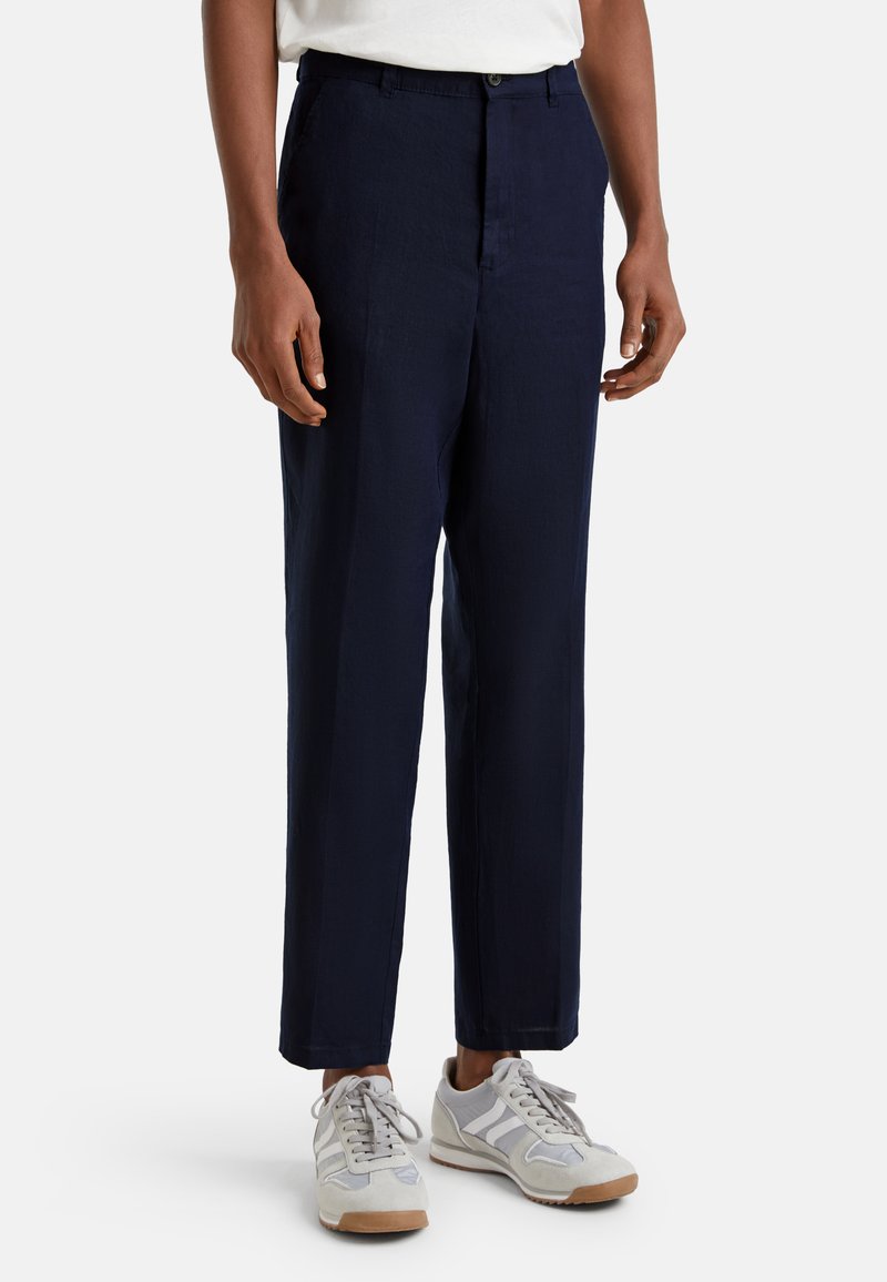 Pantalones de lino azul marino con corte recto, cierre de botón y bolsillos laterales, combinados con zapatillas deportivas de color claro.